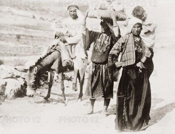 Arab family on a rural road. An Arab family travel along a rural road with two sleeping children. The women walk, and both wear traditional embroidered 'thobs'. British Mandate of Palestine (Middle East), circa 1938., Middle East, Asia.