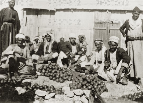 Oranges for sale, Palestine. Several Arab men sit on the ground, surrounded by heaps of oranges for sale at an outdoor market. British Mandate of Palestine (Middle East), circa 1938., Middle East, Asia.