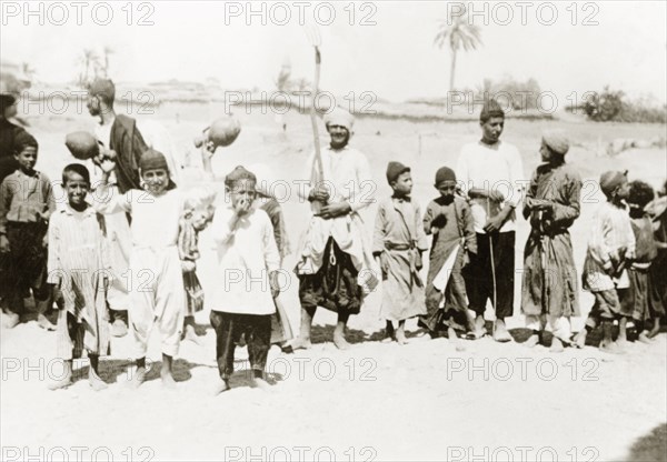 Palestinian villagers at harvest time. Men and boys stand in line with agricultural tools and gourds as they prepare to harvest the village crop. British Mandate of Palestine (Middle East), circa 1938., Middle East, Asia.