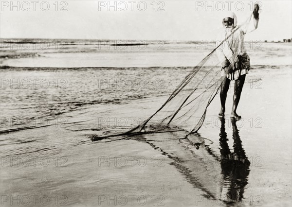 A Palestinian fisherman. An elderly Arab fisherman detangles his fishing net in shallow surf on a sandy beach. British Mandate of Palestine (Middle East), circa 1938., Middle East, Asia.