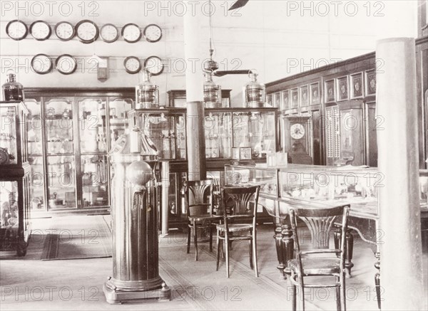 James Murray & Co.' showrooms, 1909. Interior of 'James Murray & Co.' at 12 Government Place, a British-owned family business that specialised in making chronometers and also operated as a jewellers and opticians. The showroom is filled with glass cabinets displaying watches and timepieces, with several clocks hung on the wall. Calcutta (Kolkata), India, 1909. Kolkata, West Bengal, India, Southern Asia, Asia.