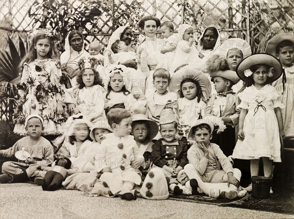 Children's fancy dress party, Calcutta 1911. Children at a fancy dress party pose for a group portrait with their carers: three Indian ayahs (nursemaids) and a smartly dressed British nanny. Calcutta (Kolkata), India, circa 1911. Kolkata, West Bengal, India, Southern Asia, Asia.