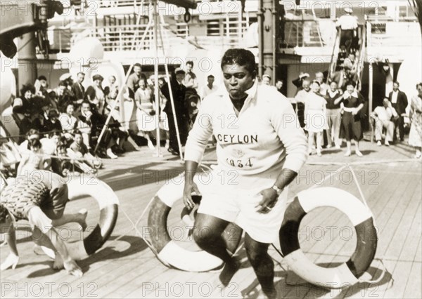 Obstacle course aboard the Otranto. Two men clamber through lifebelts as they compete in an obstacle course on the deck of the 'Otranto', a passenger liner belonging to the Orient Line. The ship was travelling from Colombo in Ceylon (Sri Lanka) to Plymouth in England. Indian Ocean, February 1939., Indian Ocean, Africa.