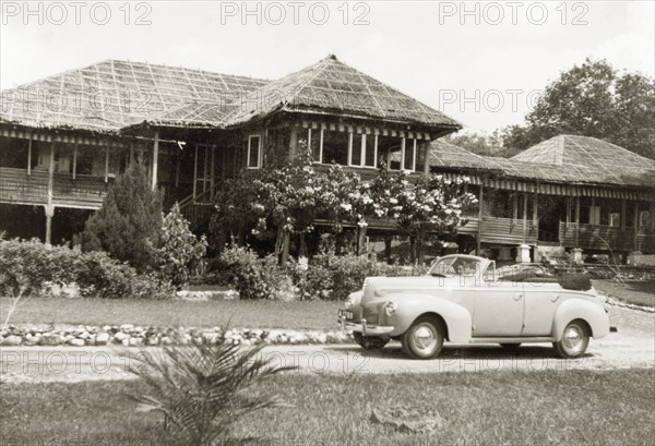 A stilted bungalow in British Malaya. A small car is parked in the driveway outside Dr Tweedie's house, a stilted bungalow with a thatched roof made from palm leaves. Sungei Siput near Ipoh, British Malaya (Malaysia), August 1940. Ipoh, Perak, Malaysia, South East Asia, Asia.