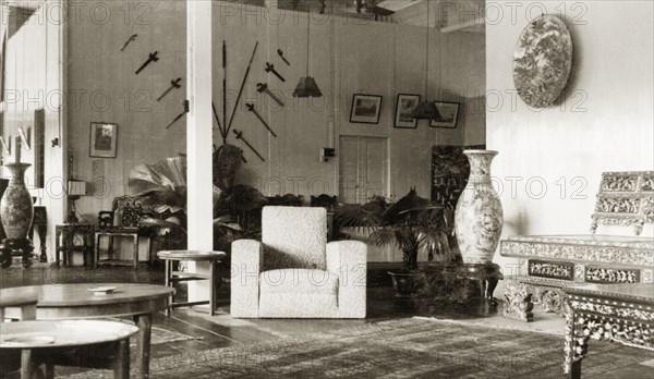 Drawing room of a colonial bungalow, British Malaya. Interior shot of a bungalow drawing room belonging to Dr Reid Tweedie. The room is furnished with a combination of Asian and British items, including a collection of axes displayed on the rear wall. Sungei Siput near Ipoh, British Malaya (Malaysia), August 1940. Ipoh, Perak, Malaysia, South East Asia, Asia.