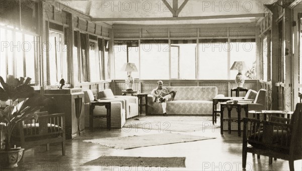 Drawing room of a colonial bungalow, British Malaya. Dr Reid Tweedie sits reading a newspaper in the sunny sitting room of his stilted bungalow. Sungei Siput near Ipoh, British Malaya (Malaysia), August 1940. Ipoh, Perak, Malaysia, South East Asia, Asia.