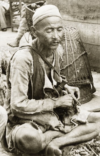 An elderly man at Darjeeling market. An elderly man sits cross-legged at a stall in Darjeeling market. Darjeeling, India, 1942. Darjeeling, West Bengal, India, Southern Asia, Asia.