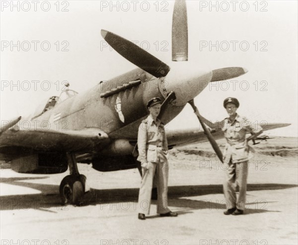 Posing beside a Supermarine Spitfire. Roland Britton (left), a fighter pilot in No. 17 Squadron of the Royal Air Force, poses beside a Supermarine Spitfire with his friend, British businessman James Murray. Murray comments that he ?made (Britton) a steel stencil (for the plane) so that the insignia, a mailed fist, could be sprayed on quickly?. Calcutta (Kolkata), India, circa 1944. Kolkata, West Bengal, India, Southern Asia, Asia.