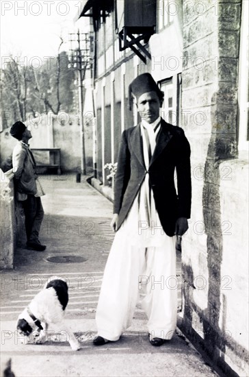 A 'Gentleman's Gentleman'. Full-length portrait of an Indian valet named Abdul, employed by British businessman James Murray who describes him as "my Gentlemen's Gentleman". He is accompanied by the Murrays' pet dog George and wears his "walking out clothes" and a fez hat. Calcutta (Kolkata), India, circa 1935. Kolkata, West Bengal, India, Southern Asia, Asia.