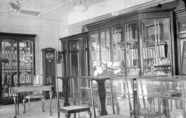James Murray & Co.' showrooms, circa 1935. Interior of 'James Murray & Co.' on Old Court House Street, a British-owned family business that specialised in making chronometers and also operated as a jewellers and opticians. The showroom is filled with glass cabinets displaying watches and timepieces, with a grandfather clock standing in the corner. Calcutta (Kolkata), India, circa 1935. Kolkata, West Bengal, India, Southern Asia, Asia.