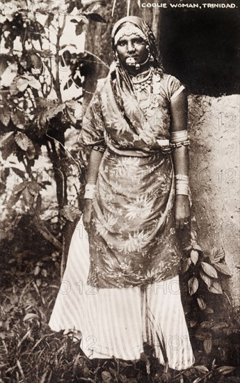 An Indo-Trinidadian woman. Full-length portrait of an Indo-Trinidadian woman, originally identified as a 'coolie'. She is dressed in a floral patterned sari and is adorned with jewellery including armbands, bangles, necklaces, a nose ring and a decorative head band. Trinidad, circa 1920., Trinidad and Tobago, Trinidad and Tobago, Caribbean, North America .