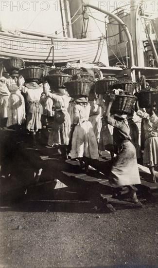 Women refueling a ship, Jamaica. A team of Jamaican women carry baskets of coal aboard a ship, as it stops to refuel at a dock in St Thomas. St Thomas, Jamaica, circa 1918., St Thomas (Jamaica), Jamaica, Caribbean, North America .