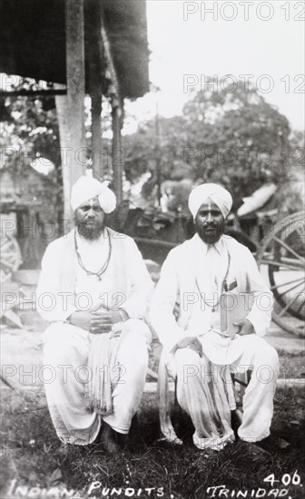 Indian 'pundits', Trinidad. Portrait of two Indian 'pundits', a term used to describe Hindu scholars or religious teachers. The men wear traditional Hindu dress, including turbans and 'tilakas' on their foreheads, and one man wears a beaded necklace, possibly 'japa mala' (prayer beads), and holds a closed book tucked under one arm. Trinidad, circa 1930., Trinidad and Tobago, Trinidad and Tobago, Caribbean, North America .