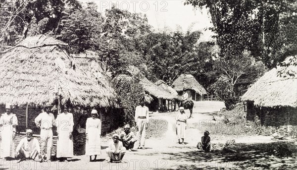 Rural Jamaican village. View of a rural Jamaican village, where residents stand outside a cluster of thatched huts which line the street. Jamaica, circa 1907. Jamaica, Caribbean, North America .