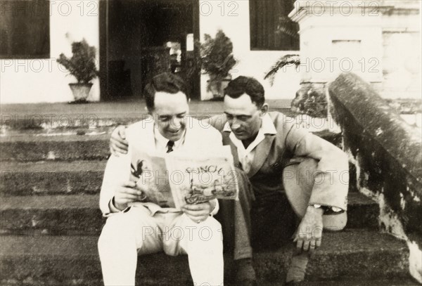 Reading 'Punch' magazine. Mr Moulton and Mr Horler sit on the steps of the United Theological College reading a copy of Punch magazine. Bangalore, India, circa 1932. Bangalore, Karnataka, India, Southern Asia, Asia.