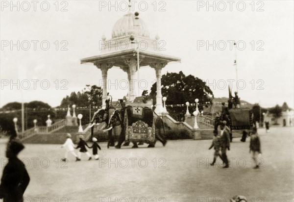 Elephant procession at Dasara Festival. Caparisoned elephants parade past a monument in Mysore during a procession for the Dasara Festival, a Hindu celebration to mark the triumph of Lord Rama over demon King Ravana. Mysore, India, 1933. Mysore, Karnataka, India, Southern Asia, Asia.