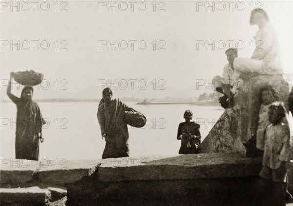 Women at a lakeside ghat, India. Women carry loaded baskets up a ghat (stepped wharf) after washing the contents in a lake. Tumkur, Mysore State (Tumakuru, Karnataka), India, circa 1933., Karnataka, India, Southern Asia, Asia.