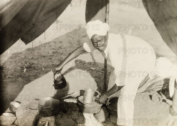 Methodist missionary camp site. A Methodist evangelist called Simon pours water from a kettle into a cooking pot over a camp fire. Simon was accompanying British missionary Reverend Norman Sargant, who travelled throughout Mysore State preaching to rural Christian communities. Mysore State (Karnataka), India, 1933., Karnataka, India, Southern Asia, Asia.