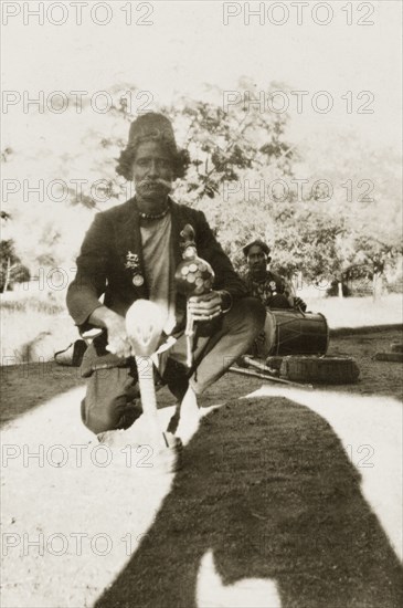 Indian snake charmer. An Indian snake charmer poses for the camera with a coiled up cobra positioned in a basket in front of him. He holds a 'pungi' in one hand, a musical instrument made from bamboo that is traditionally used in the art of snake charming. Mysore state (Karnataka), India, circa 1933., Karnataka, India, Southern Asia, Asia.