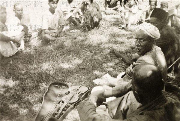 Evangelist preaching to plantation workers. A Methodist evangelist called D. Anniah sits in a circle with a group of plantation workers, his violin positioned in an open case beside him. D. Anniah was accompanying British missionary Reverend Norman Sargant, who travelled throughout Mysore State preaching to rural Christian communities. Mysore State (Karnataka), India, 1934., Karnataka, India, Southern Asia, Asia.