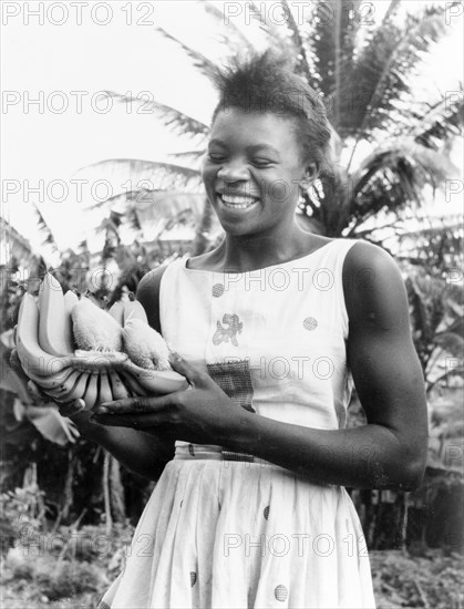 Antiguan woman with bananas. A young Antiguan woman smiles broadly as she displays a bunch of bananas for the camera. Antigua, 1965. Antigua and Barbuda, Caribbean, North America .