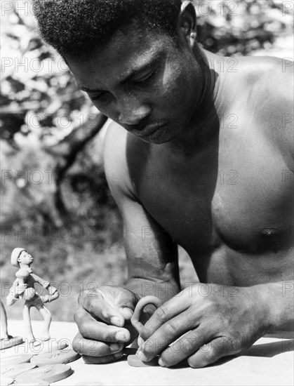An Antiguan craftsman. A young Antiguan craftsman concentrates as he models small figurines out of clay. Antigua, 1965., Antigua and Barbuda, Caribbean, North America .