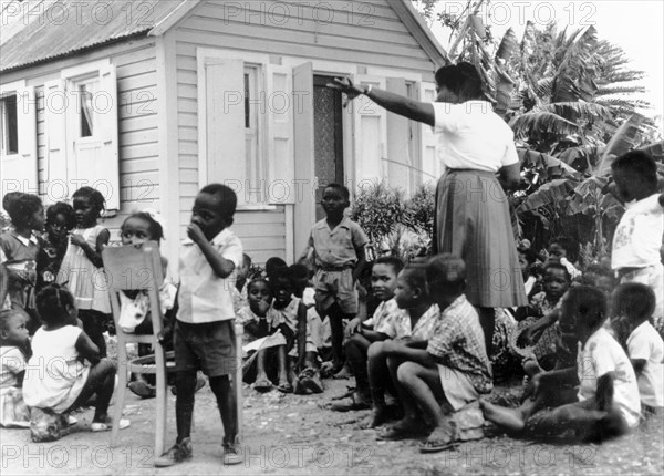 An outdoor classroom in Antigua. An Antiguan teacher oversees a group of schoolchildren outside a tiny school building. Antigua, 1965., Antigua and Barbuda, Caribbean, North America .