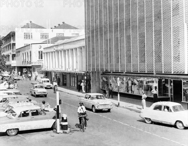 The main street, Bridgetown. Traffic and pedestrians travel along the main street of Bridgetown in front of modern shops with window displays. Bridgetown, Barbados, 1965. Bridgetown, St Michael, Barbados, Caribbean, North America .