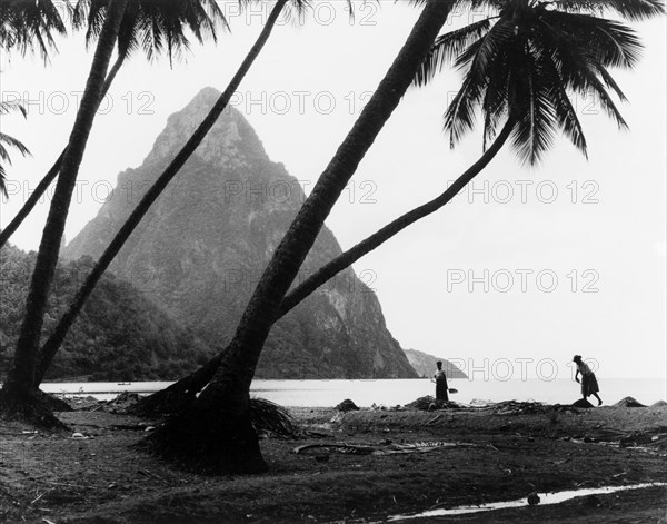 The Pitons, St Lucia. One of the Pitons rises up from the coastline of St Lucia, behind a beach of silhouetted palm trees. St Lucia, 1965., St Lucia, Caribbean, North America .