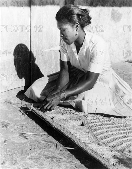 Weaving a palm mat, Dominica. A young woman sits on the ground as she weaves a mat from palm fibre. Dominica, 1965. Dominica, Caribbean, North America .