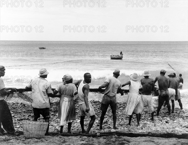 Hauling in the nets, Granada. A line of men and women haul in their fishing nets on a sandy beach in Grenada. Grenada, 1965. Grenada, Caribbean, North America .