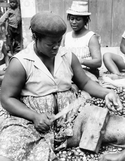 Shelling a nutmeg harvest. A Grenadian woman uses a tool to crack open nutmeg shells against a wooden brick. Grenada, 1965. Grenada, Caribbean, North America .