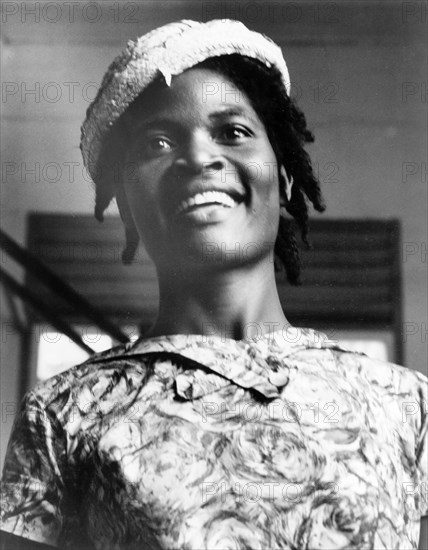 Portrait of a Grenadian woman. Head and shoulders portrait of a young Grenadian woman, dressed smartly in a patterned dress and woven hat with her hair in braids. Grenada, 1965. Grenada, Caribbean, North America .