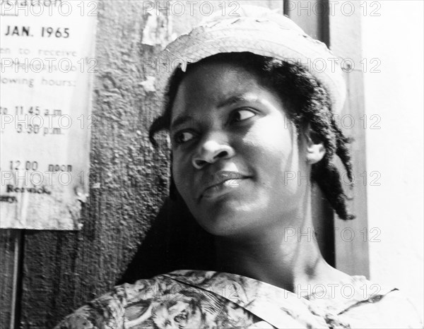 Portrait of a Grenadian woman. Portrait of a young Grenadian woman, dressed smartly in a patterned dress and woven hat with her hair in braids. Grenada, 1965. Grenada, Caribbean, North America .