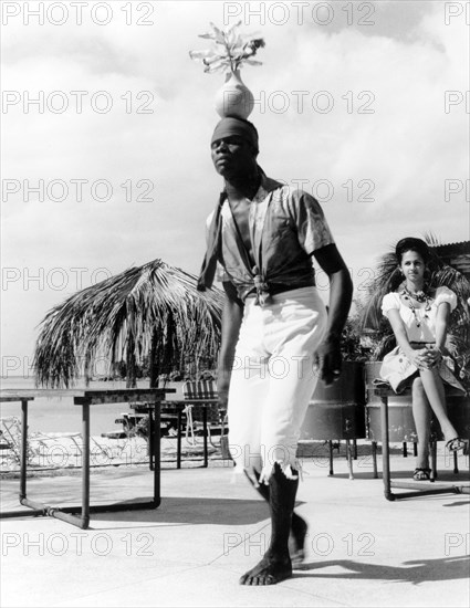 A limbo dancer in Grenada. A Grenadian man balances a vase of flowers on his head as he performs a limbo dance at a tourist beach resort. Grenada, 1965., Grenada, Caribbean, North America .