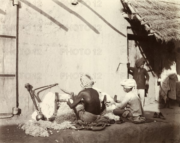 Indian cotton weavers. Two Indian men sit weaving cotton on the ground outside a mud-walled building. United Provinces (Uttar Pradesh), India, January 1903., Uttar Pradesh, India, Southern Asia, Asia.