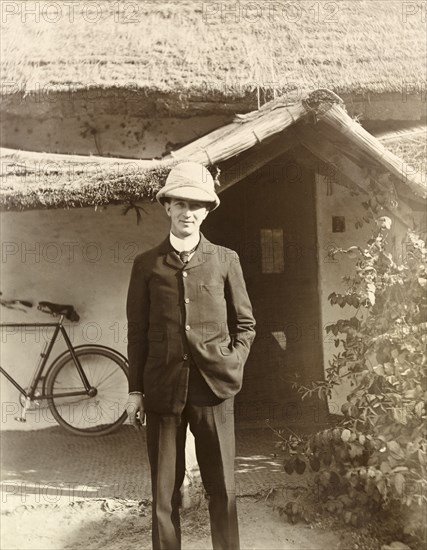 Man posing by thatched cottage, India. Portrait of a European man posing outside a thatched cottage with a woven front door. Assam, India, 1903., Assam, India, Southern Asia, Asia.