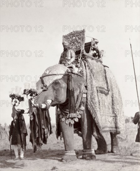 Caparisoned state elephant of Alwar. The caparisoned state elephant of Alwar carries an ornate howdah on its back during a procession at the Coronation Durbar. The elephant is decorated with an ornamental headpiece, beads strung round its neck, and two chandeliers fixed upon the tip of each tusk. Delhi, India, circa 1 January 1903. Delhi, Delhi, India, Southern Asia, Asia.