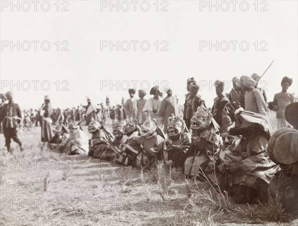 Masked 'devil dancers' at Coronation Durbar, 1903. A group of 'lamas' (Buddhist monks) sit in a row on the ground wearing large, elaborate masks, as they prepare to perform a 'devil dance' at the Coronation Durbar. Delhi, India, circa 1 January 1903. Delhi, Delhi, India, Southern Asia, Asia.