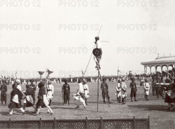 Performers at Coronation Durbar, 1903. Performers from Kutch State enter the pavilion arena at Edward VII's Coronation Durbar. Amongst the group of performers are musicians playing silver trumpets and a stilt walker. Delhi, India, circa 1 January 1903. Delhi, Delhi, India, Southern Asia, Asia.