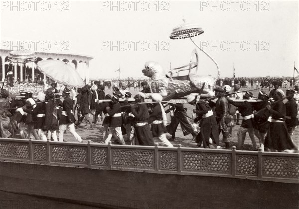 Lion-shaped carriage at Coronation Durbar, 1903. A silver, lion-shaped carriage from Kutch State is carried by Indian bearers into the pavilion arena at Edward VII's Coronation Durbar. An original caption comments that the 'tail (of the lion) form(s) an umbrella.' Delhi, India, circa 1 January 1903. Delhi, Delhi, India, Southern Asia, Asia.