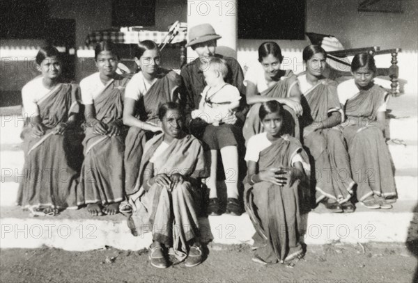 Chikmagalur Girl Guides. Group portrait of the Chikmagalur Girl Guides seated on the steps of a veranda with troop leader Joan Sargant. The girls wear a uniform of traditional saris over a white 'choli' (blouse), while Joan Sargant wears a Western-style scouting uniform and sits cuddling her baby daughter Nell. Chikmagalur, Mysore State (Chikkamagaluru, Karnataka), India, circa 1937., Karnataka, India, Southern Asia, Asia.