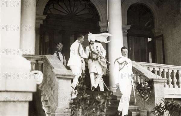 Departing the Prime Minister of Indore's palace. British and Indian officers dressed in full military regalia descend the front steps of the Prime Minister of Indore's palace. The group had been attending a garden party held in honour of a visit by Lord Irwin, Viceroy of India. Indore, Indore State (Madhya Pradesh), India, 2 August 1928. Indore, Madhya Pradesh, India, Southern Asia, Asia.