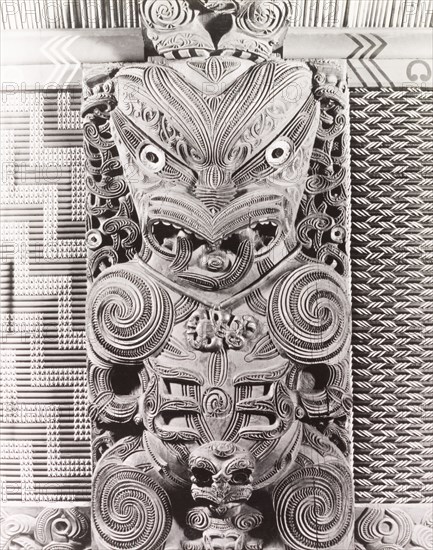 Maori 'tekoteko' panel. Close-up shot of a Maori 'tekoteko' panel, a human-like figure carved from wood and elaborately decorated with swirling patterns. An original caption comments: "(This) panel is in the interior of the Tamtekapu meeting house in Rotorua". Rotorua, New Zealand, 1966. Rotorua, Bay of Plenty, New Zealand, New Zealand, Oceania.