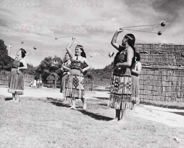 Maori women perform the 'double long poi'. A group of Maori women perform the 'double long poi', a form of juggling using balls attached to ropes. They wear traditional Maori dress including 'piupius' (woven flax skirts) and 'tipares' (headbands). Near Rotorua, New Zealand, 1966. Rotorua, Bay of Plenty, New Zealand, New Zealand, Oceania.