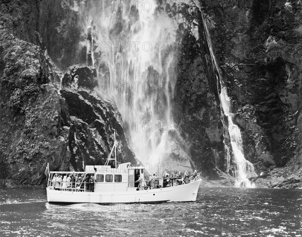 A tourist launch at Milford Sound. A launch carrying tourists cruises past a waterfall at Milford Sound. Southland, New Zealand, 1966., Southland, New Zealand, New Zealand, Oceania.