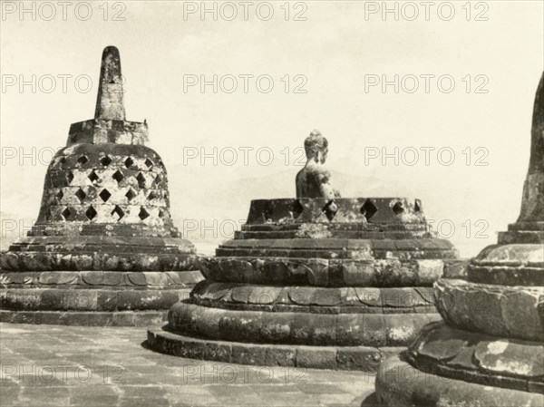 Statues of the Buddha at Borobudur. Bell-shaped stupas at the ninth century Buddhist monument of Borobudur, each containing statues of the Buddha seated in the lotus position. Java, Indonesia, July 1940., Java, Indonesia, South East Asia, Asia.