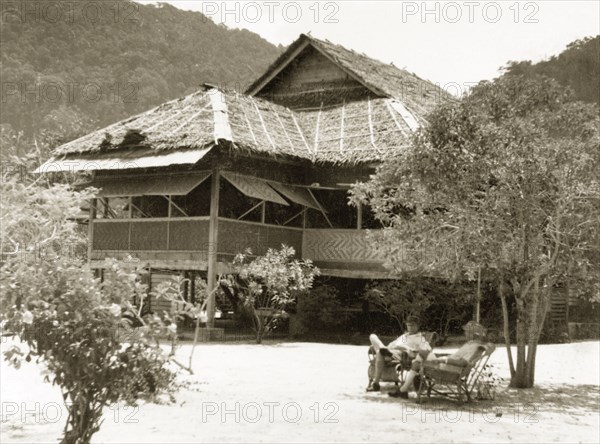 A weekend residence on Pangkor Island. Two European men relax in chairs outside a stilted bungalow on the beach, the weekend residence of Dr Reid Tweedie. Pangkor Island, British Malaya (Malaysia), 1940. Pangkor Island, Perak, Malaysia, South East Asia, Asia.