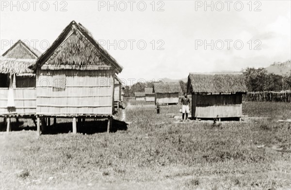 New housing, North Borneo. View of a row of new stilted, bamboo houses with accompanying outhouses. The buildings were built by North Borneo Medical Services as part of a health campaign to introduce new hygiene and sanitation practices to local villages. Keningau, North Borneo (Sabah, Malaysia), circa 1937. Keningau, Sabah (North Borneo), Malaysia, South East Asia, Asia.
