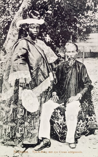 Creole woman with Asian husband, Suriname. Portrait of a creole woman posing next to her East Asian husband on a street in Suriname. Paramaribo, Suriname, circa 1910. Paramaribo, Suriname, Suriname, South America, South America .